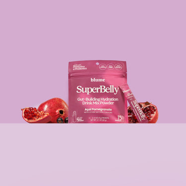 Acai Pomegranate Superbelly hydration drink mix package with fresh acai berries and cut up pomegranate fruit on a purple background