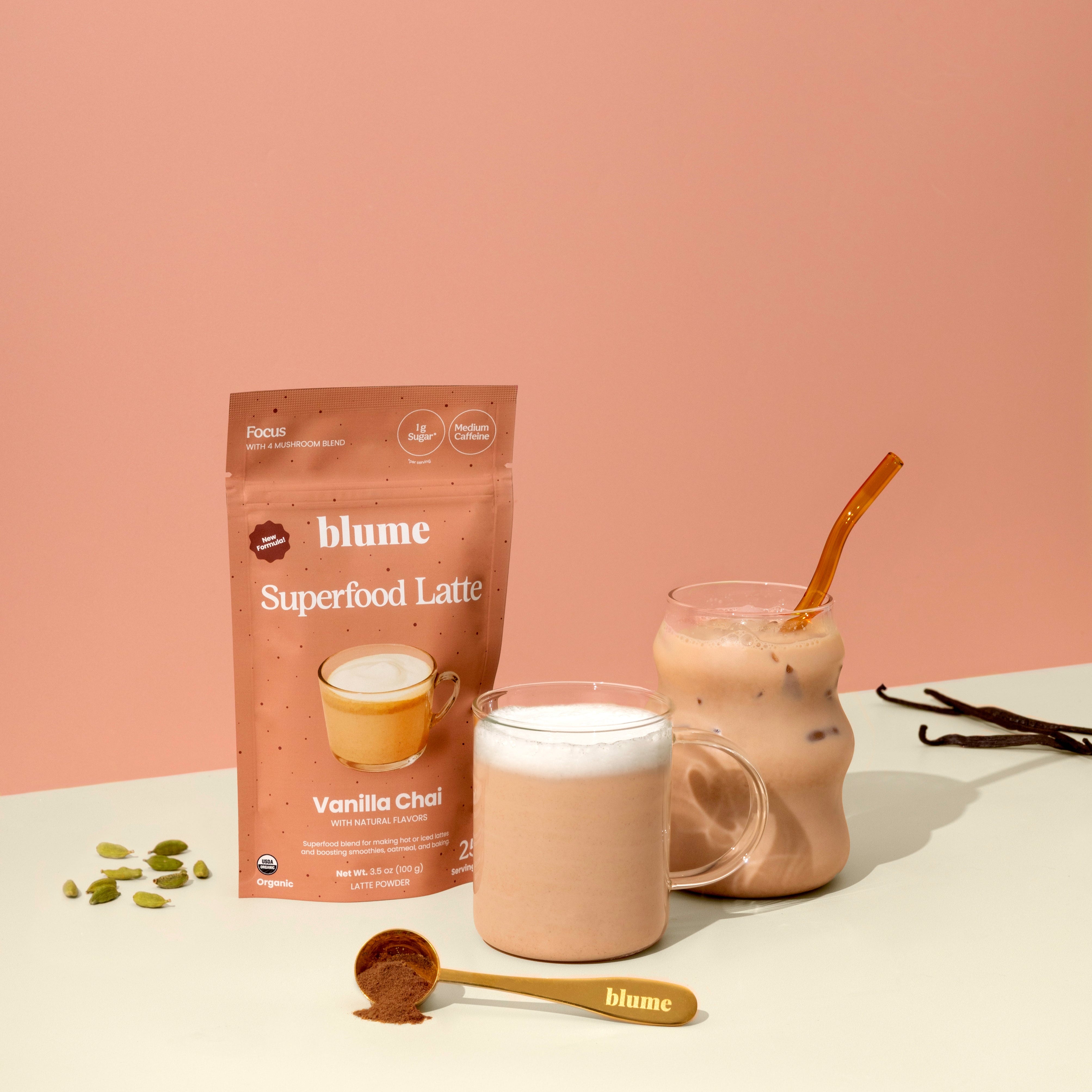 A packaged product labeled 'Blume Superfood Latte' in Vanilla Chai flavor, alongside a prepared latte in a cup with a spoon on the side, against a pink background.