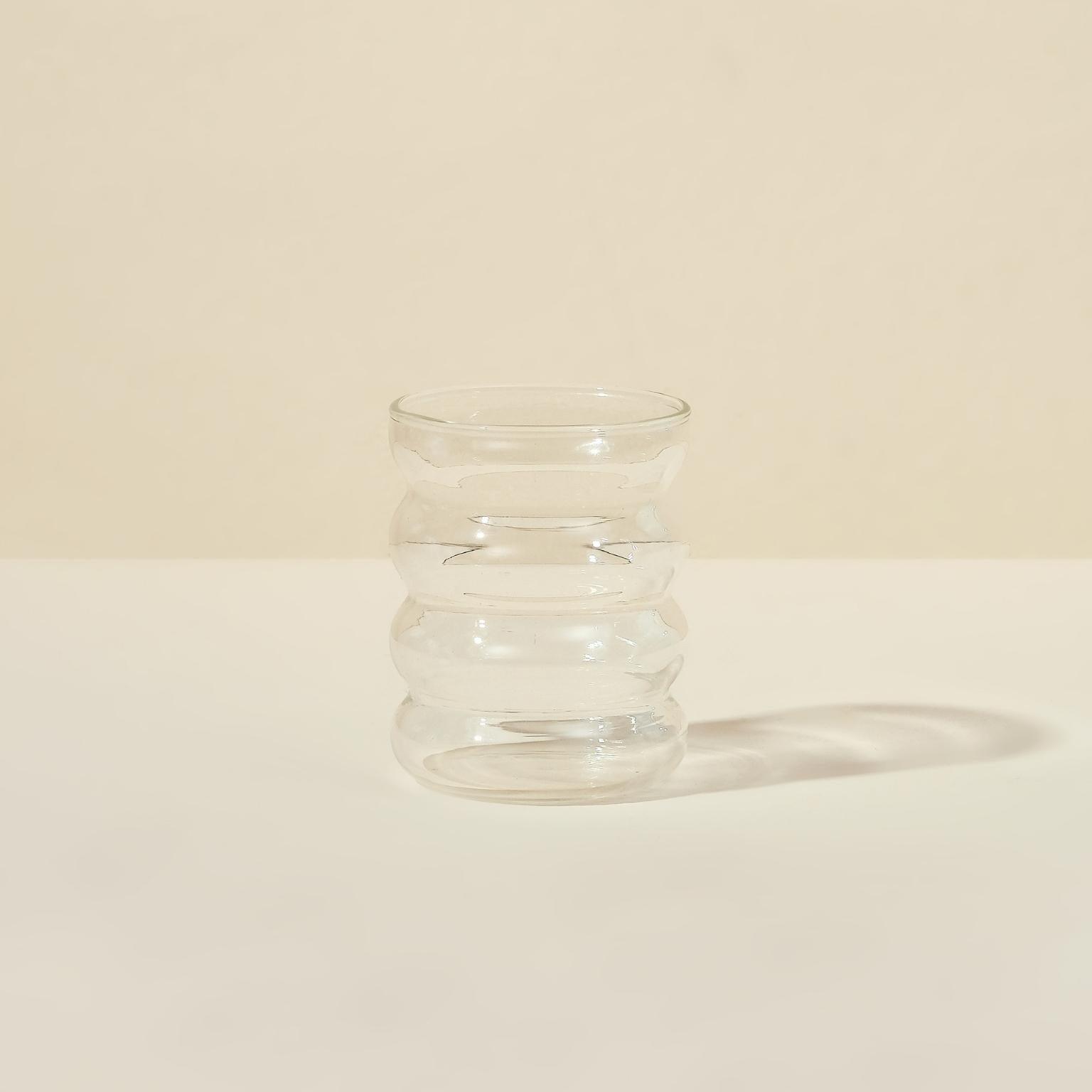 The Blume Bubble Cup, with its distinct wavy-patterned bubble glass, rests on a light beige background. Its unique curves highlight vibrant smoothies while casting subtle shadows beneath it.