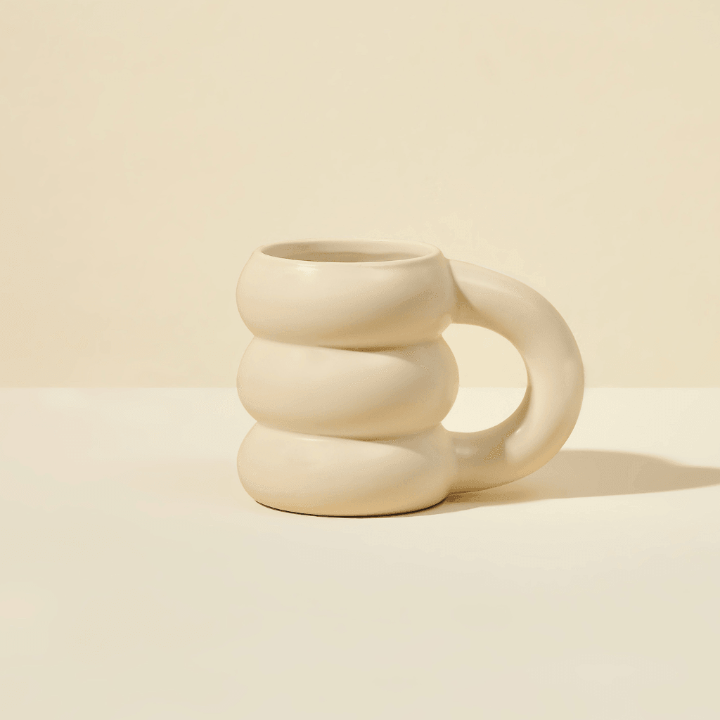 The limited edition Cloud Mug by Blume features a cream-colored ceramic design with a unique wavy spiral and oversized handle, set against a light beige background, adding an artistic touch to any collection.