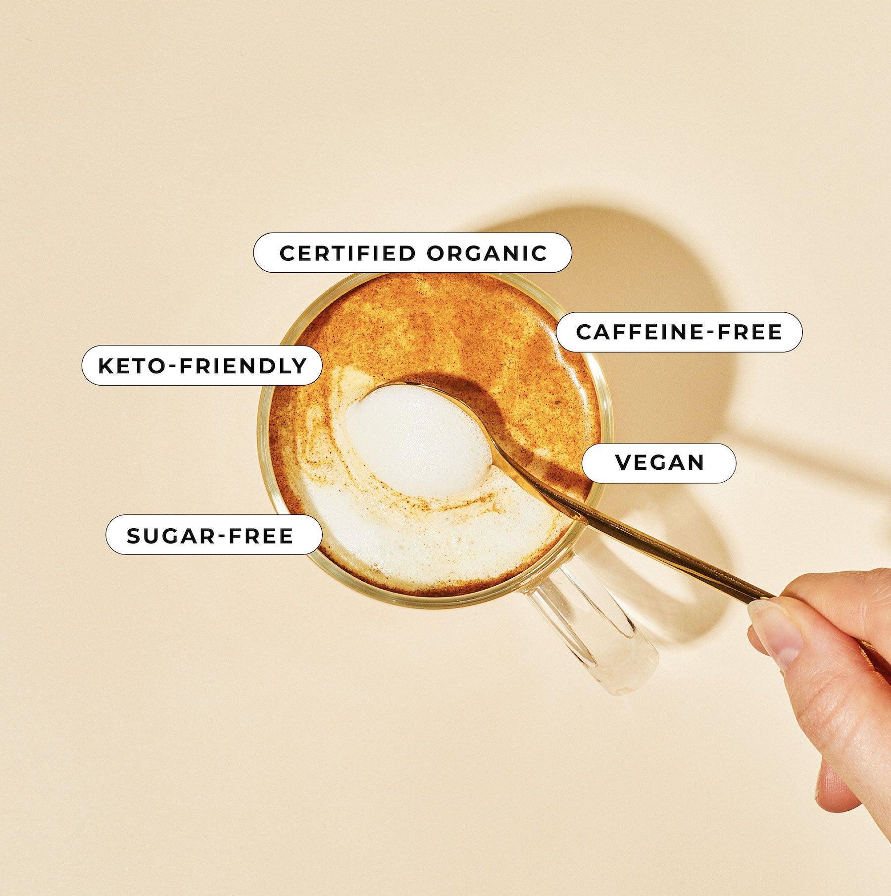 A hand stirs a frothy coffee cup on a light surface, decorated with tags: Certified Organic, Caffeine-Free, Keto-Friendly, Golden Mylk, and Vegan. Blumes Turmeric Blend, rich in super-spices, provides a delightful twist to your daily brew.