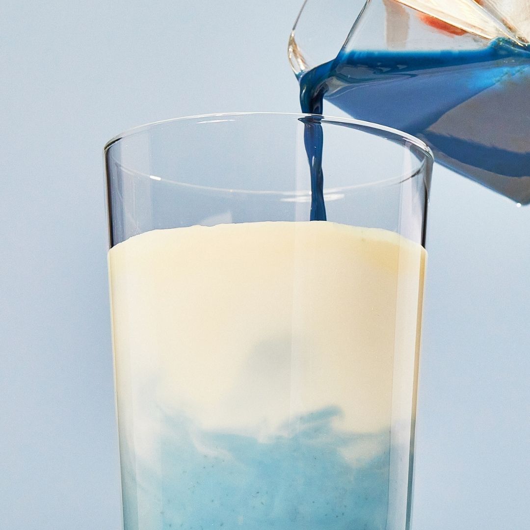 Blue Lavender Blend mixture pouring into a glass cup of milk on a blue background