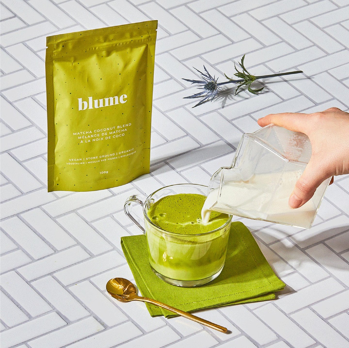 Milk pouring into a glass mug of matcha latte made with Blume Matcha Coconut Blend on a tile background