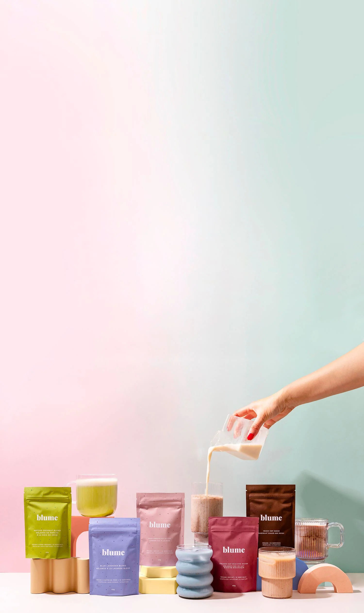 A hand pours milk into a transparent cup with powder. Various colorful packets and mugs are lined up on a white surface against a pastel gradient background. Items include green, pink, purple, and brown packages, some labeled Blume.