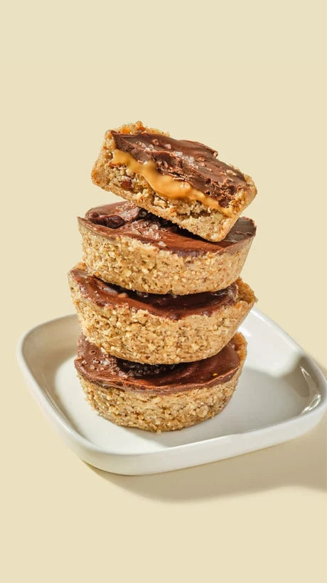 A stack of four dessert cups with oatmeal bases and chocolate tops. The top cup is cut in half, revealing a layer of creamy caramel. The desserts are placed on a small white dish against a light beige background.