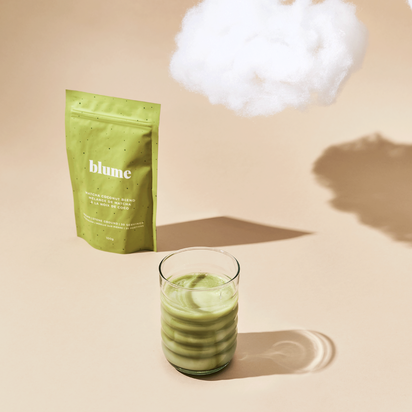 A glass of matcha latte made with Blume Matcha Coconut Blend on a beige background with a cloud