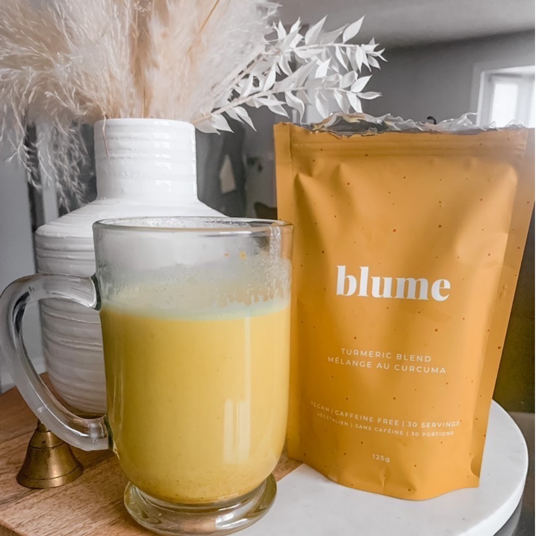 Turmeric latte in a glass mug with a bag of Blume Turmeric Blend in a living room taken by @explore_withfood