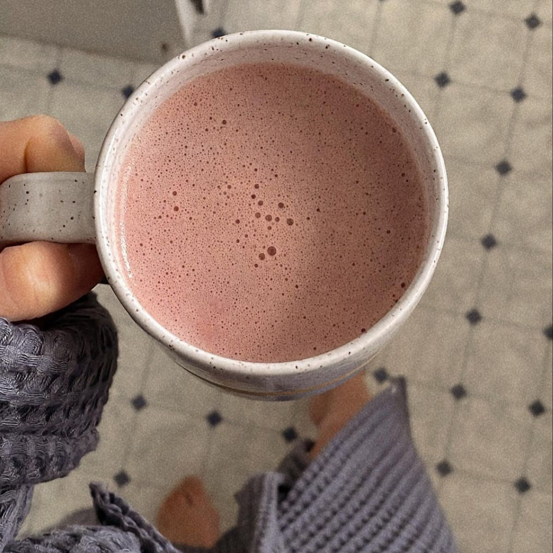 Holding a mug of Blume's Beetroot Latte in the kitchen taken by Blume's Matcha Coconut Latte pouring into a glass cup filled with ice cubes taken by @gabrielleassaf