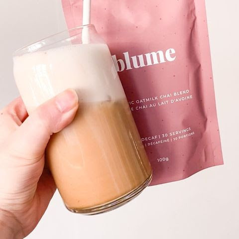 Holding a glass cup of iced chai latte and a bag of Blume Oat Milk Chai Blend taken by @itstheveganbean