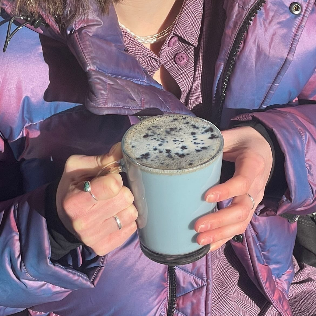 A glass mug of Blume's Blue Lavender Latte taken by @piecesofsarah with a purple puffer jacket