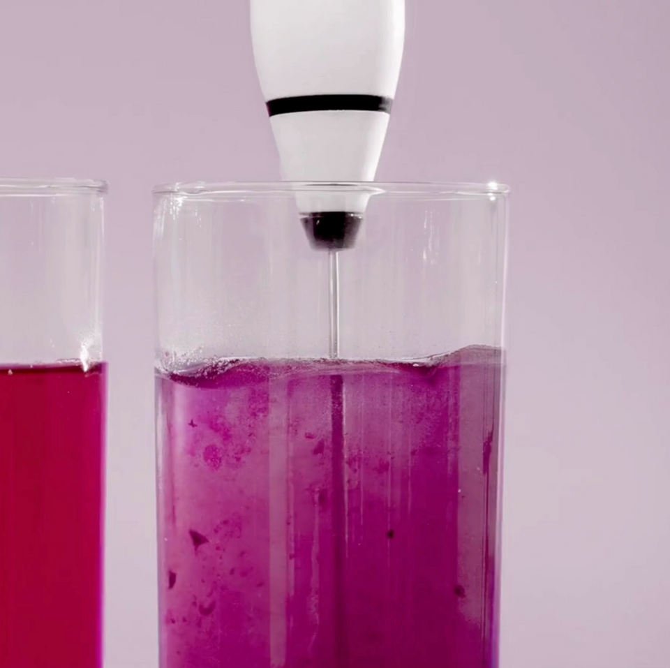 Whisking SuperBelly in a glass with Blume's white 3-speed whisk on a pink background