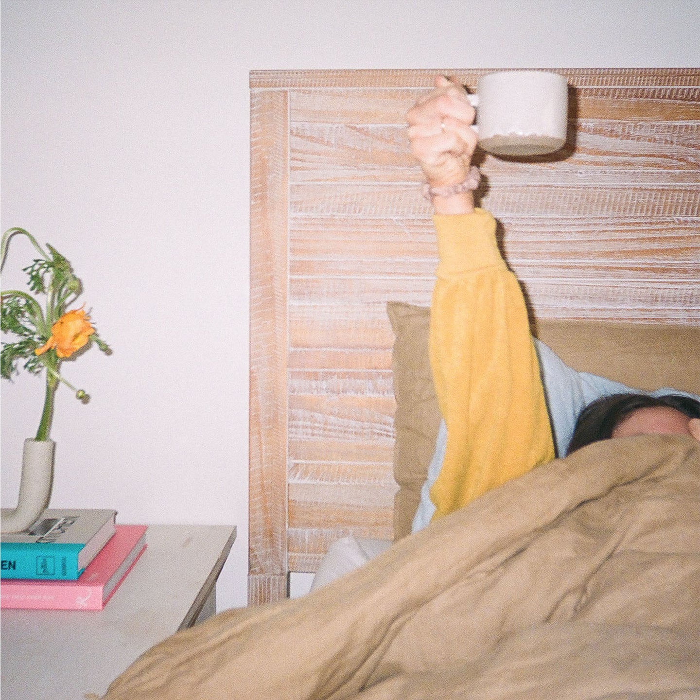 A girl raising a cup of a latte in the bed